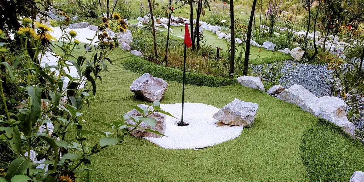 Rupa s crvenom zastavicom na stazi mini golfa u Eko Golf Parku, okružena kamenjem i cvijećem